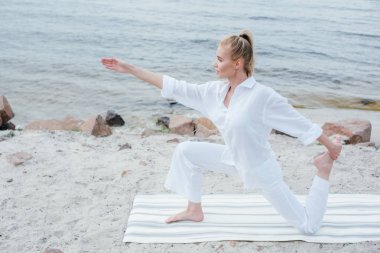 deniz kenarında yoga yapan çekici sarışın genç kadın 