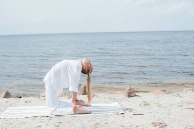 deniz kenarında yoga minderi üzerinde yoga yapan kapalı gözlü güzel kadın 
