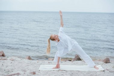 deniz kenarında yoga minderi üzerinde yoga yapan kapalı gözlü çekici kız 