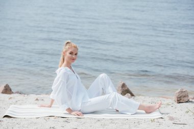 nehir yakınında yoga mat üzerinde oturan neşeli sarışın genç kadın 