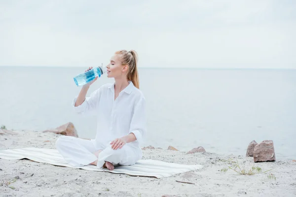 Attraktive Frau Sitzt Auf Yogamatte Und Hält Sportflasche Während Sie — Stockfoto