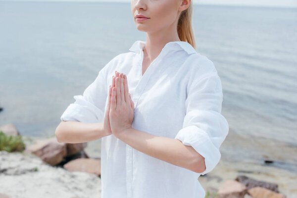 обрезанный вид молодой женщины с молящимися руками у моря
 