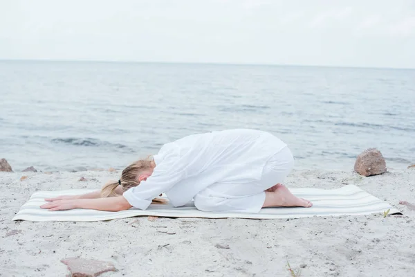 金发年轻女子放松和练习瑜伽垫附近的海 — 图库照片