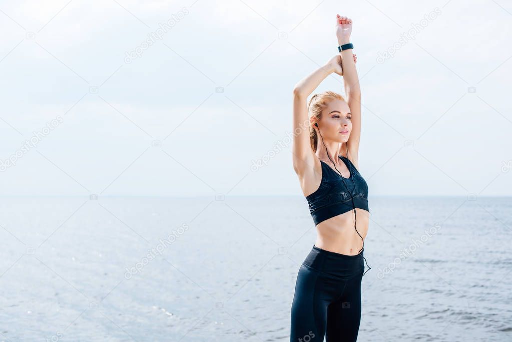 beautiful athletic girl stretching and listening music in earphones near sea 