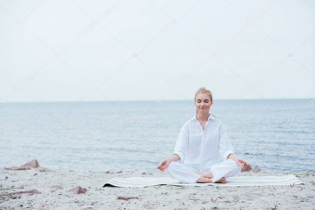 happy blonde young woman with closed eyes sitting on yoga mat 