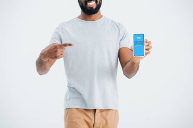 KYIV, UKRAINE - MAY 17, 2019: cropped view of african american man pointing at smartphone with skype app, isolated on grey  clipart