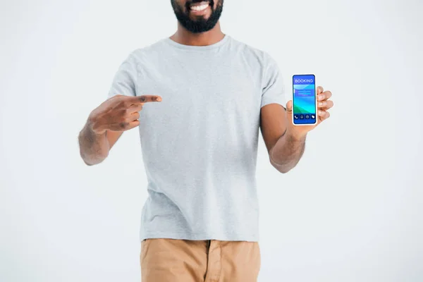 予約アプリでスマートフォンを指すアフリカ系アメリカ人男性のトリミングされたビュー 灰色で隔離 — ストック写真