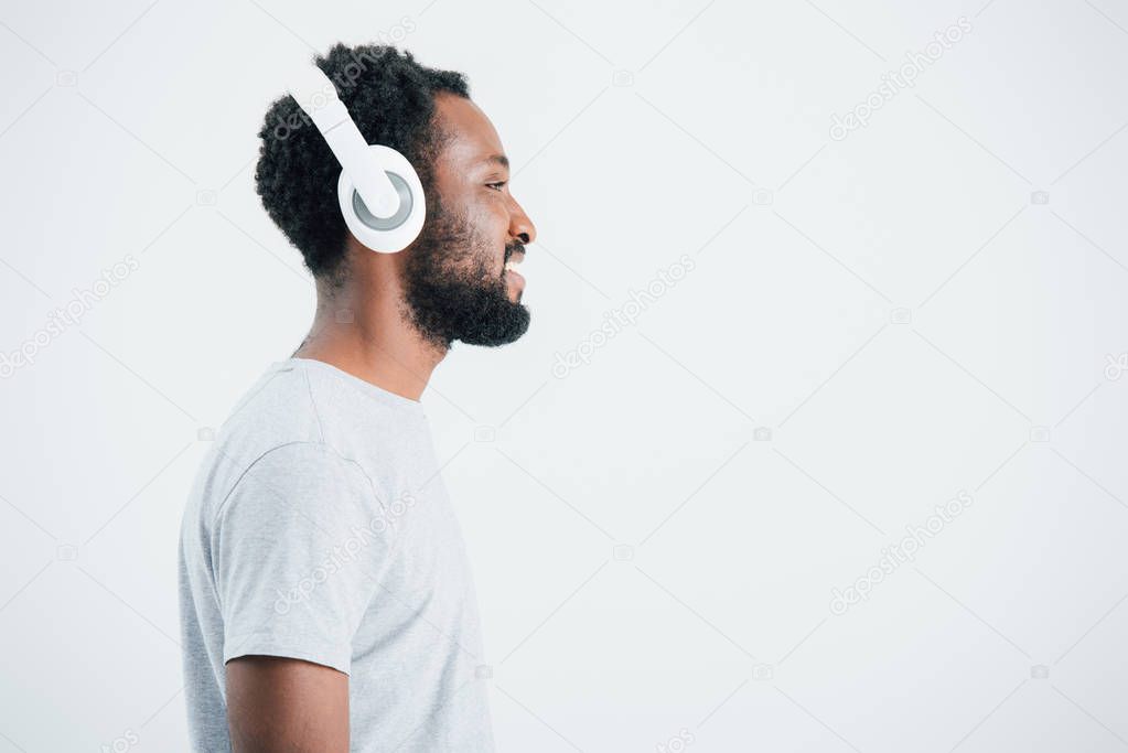 happy african american man listening music with headphones, isolated on grey