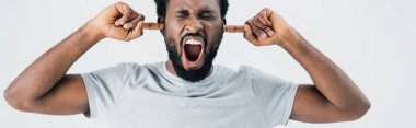 emotional african american man in grey t-shirt yelling and closing ears isolated on grey clipart