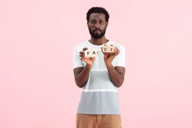 african american man holding alphabet cubes with fact word, isolated on pink clipart