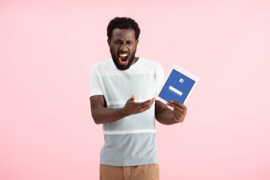 Kiev, Ukrayna - 17 Mayıs 2019: duygusal afro-amerikan adam bağırarak ve facebook uygulaması ile dijital tablet gösteren, pembe izole
