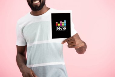 Kiev, Ukrayna - 17 Mayıs 2019: pembe izole deezer uygulaması ile dijital tablet gösteren Afrikalı Amerikalı adam kırpılmış görünümü