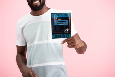 pembe izole rezervasyon uygulaması ile dijital tablet gösteren gülümseyen afrikalı amerikalı adam kırpılmış görünümü