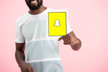 Kiev, Ukrayna - 17 Mayıs 2019: Snapchat uygulaması ile dijital tablet gösteren Afrikalı Amerikalı adamın kırpılmış görünümü, pembe izole