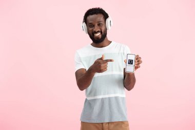 Kiev, Ukrayna - 17 Mayıs 2019: Afro-Amerikan adam kulaklıkla müzik dinliyor ve pembe yebağlı uber uygulamasıyla akıllı telefonu işaret ediyor 