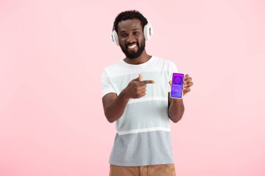 afro-amerikan adam kulaklık ile müzik dinleme ve alışveriş uygulaması ile akıllı telefon işaret, pembe izole 