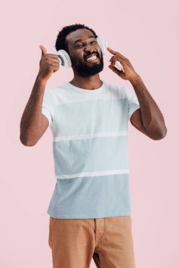 neşeli afro-amerikan adam kulaklık ile müzik dinleme ve başparmak gösteren, pembe izole