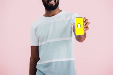 KYIV, UKRAINE - MAY 17, 2019: cropped view of african american man showing smartphone with Snapchat app, isolated on pink  clipart