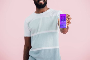 alışveriş uygulaması ile akıllı telefon gösteren Afrikalı-Amerikalı adam kırpılmış görünümü, pembe izole 