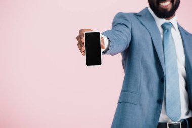 boş ekranlı akıllı telefon tutan Afrikalı-Amerikalı işadamının kırpılmış görünümü, pembe izole