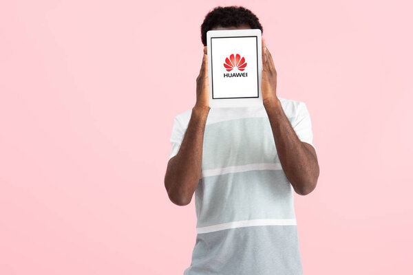 KYIV, UKRAINE - MAY 17, 2019: african american man shouting and showing digital tablet with huawei app, isolated on pink