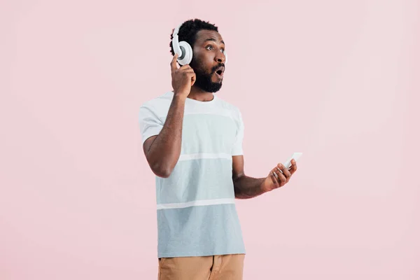 ヘッドフォンとスマートフォンで音楽を聴く興奮したアフリカ系アメリカ人男性 ピンクで隔離 — ストック写真