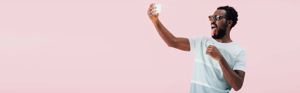 サングラスをかけたアフリカ系アメリカ人男性がスマートフォンで自分撮りをする ピンクで孤立 — ストック写真