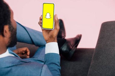 Kiev, Ukrayna - 17 Mayıs 2019: Beyaz letmenin koltukta oturan ve snapchat uygulaması ile akıllı telefon gösteren, pembe izole görünümü kırpılmış