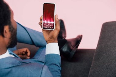 ticaret kursları ile akıllı telefon gösteren Afrikalı Amerikalı işadamının kırpılmış görünümü, pembe izole
