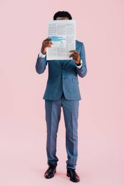 young african american businessman reading newspaper isolated on pink