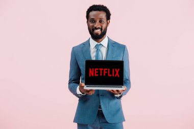 Kiev, Ukrayna - 17 Mayıs 2019: netflix web sitesi ile dizüstü bilgisayar gösteren gülümseyen Afrikalı Amerikalı işadamı, pembe izole