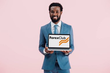Kiev, Ukrayna - 17 Mayıs 2019: gülümseyen Afrikalı Amerikalı işadamı forex club web sitesi ile dizüstü bilgisayar gösteren, pembe izole