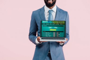 mavi izole spor bahis web sitesi ile dizüstü bilgisayar gösteren gülümseyen Afrikalı Amerikalı işadamı kırpılmış görünümü