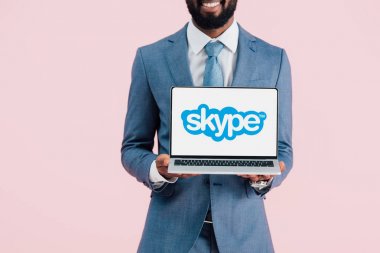 Kiev, Ukrayna - 17 Mayıs 2019: gülümseyen Afrikalı Amerikalı işadamının kırpılmış görünümü skype ile dizüstü bilgisayar gösteren, pembe izole