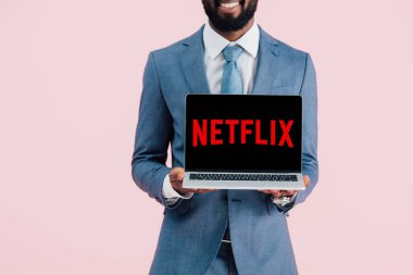 Kiev, Ukrayna - 17 Mayıs 2019: netflix web sitesi ile dizüstü bilgisayar gösteren gülümseyen Afrikalı Amerikalı işadamı kırpılmış görünümü, pembe izole