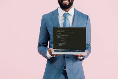 KYIV, UKRAINE - MAY 17, 2019: cropped view of smiling african american businessman showing laptop with html code, isolated on pink clipart