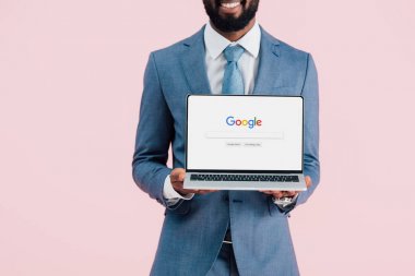Kiev, Ukrayna - 17 Mayıs 2019: gülümseyen Afrikalı Amerikalı işadamı google web sitesi ile dizüstü bilgisayar gösteren kırpılmış görünümü, pembe izole