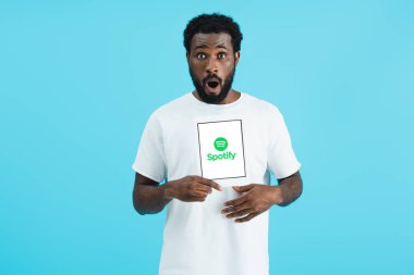 Kiev, Ukrayna - 17 Mayıs 2019: Spotify uygulaması ile dijital tablet gösteren şok Afrikalı Amerikalı adam, mavi izole