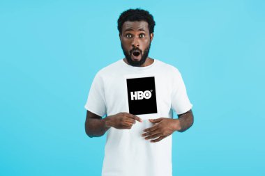 Kiev, Ukrayna - 17 Mayıs 2019: Hbo uygulaması ile dijital tablet gösteren şok Afrikalı Amerikalı adam, mavi izole