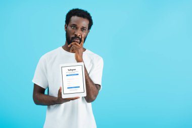Kiev, Ukrayna - 17 Mayıs 2019: düşünceli afro-amerikan adam instagram uygulaması ile dijital tablet gösteren, mavi izole