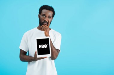 Kiev, Ukrayna - 17 Mayıs 2019: hbo uygulaması ile dijital tablet gösteren düşünceli Afrikalı Amerikalı adam, mavi izole