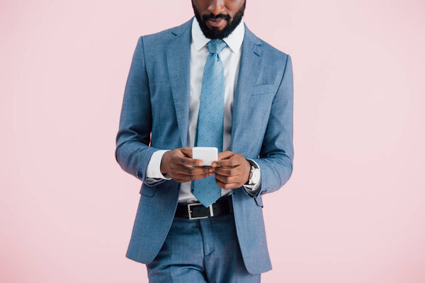 cropped view of african american businessman using smartphone, isolated on pink  