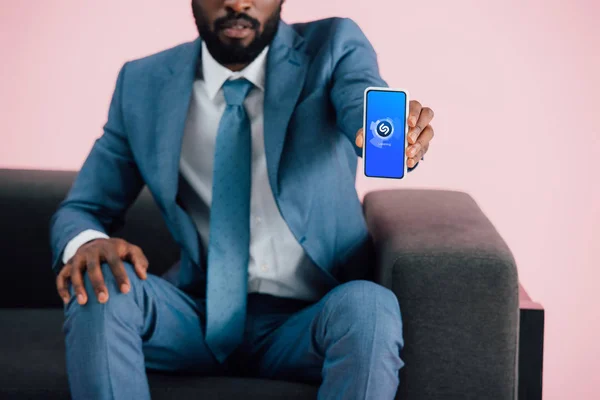乌克兰 2019年5月17日 非洲裔美国商人坐在扶手椅上 展示智能手机与Shazam应用程序 孤立的粉红色裁剪视图 — 图库照片
