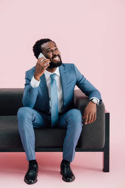 腕掛け椅子に座ってスマートフォンで話すスーツを着たアフリカ系アメリカ人のビジネスマン ピンクで孤立 — ストック写真