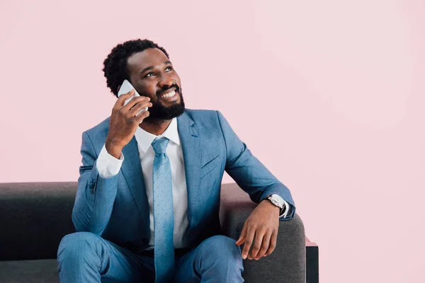 ハンサムなアフリカ系アメリカ人のビジネスマンがアームチェアに座り スマートフォンで話し ピンクで孤立 — ストック写真