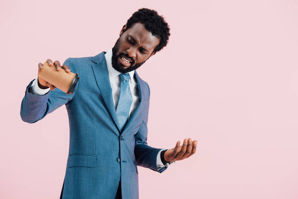 stressed african american businessman holding empty disposable cup of coffee, isolated on pink