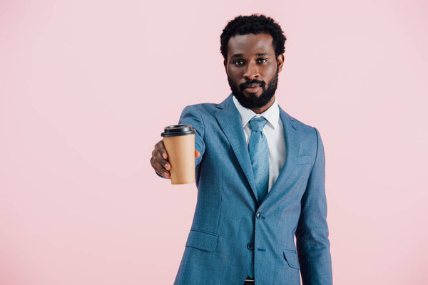 serious african american businessman holding coffee to go, isolated on pink