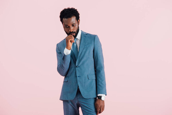 pensive african american businessman in suit, isolated on pink