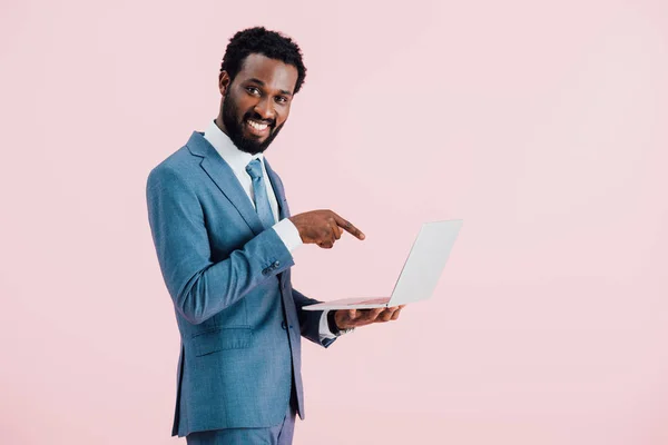 ピンクに隔離されたラップトップを指す陽気なアフリカ系アメリカ人ビジネスマン — ストック写真
