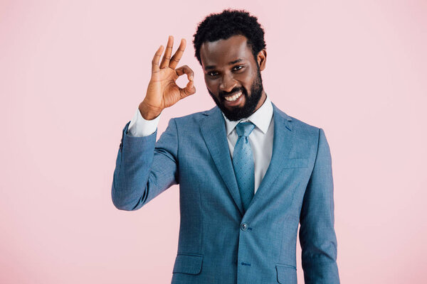 smiling african american businessman in suit showing ok sign, isolated on pink